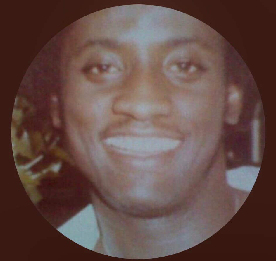 Close-up circular portrait of a smiling Black man with a thin mustache and short hair.